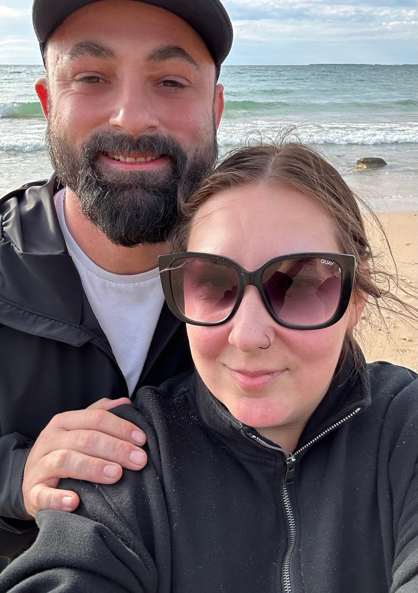 Ian and a woman in sunglasses smiling in a selfie on a beach.