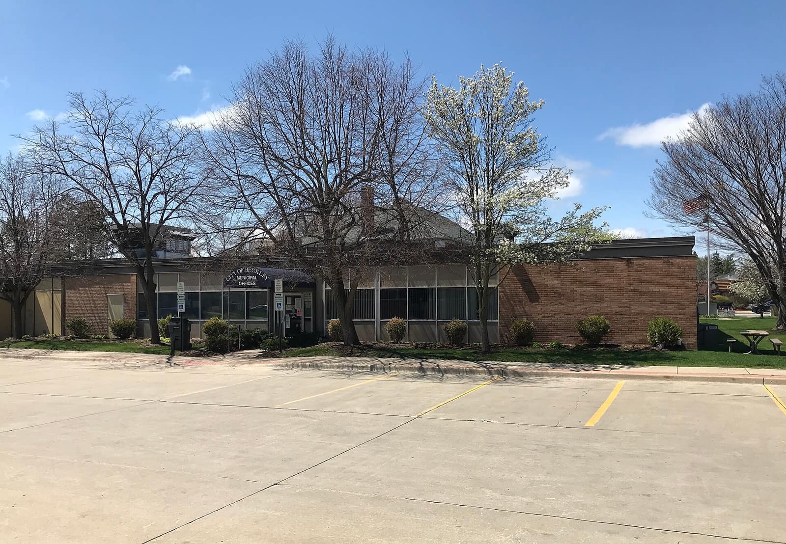 Berkley City Hall, a low brick municipal building with a flagpole and spring trees, seen from the parking lot.
