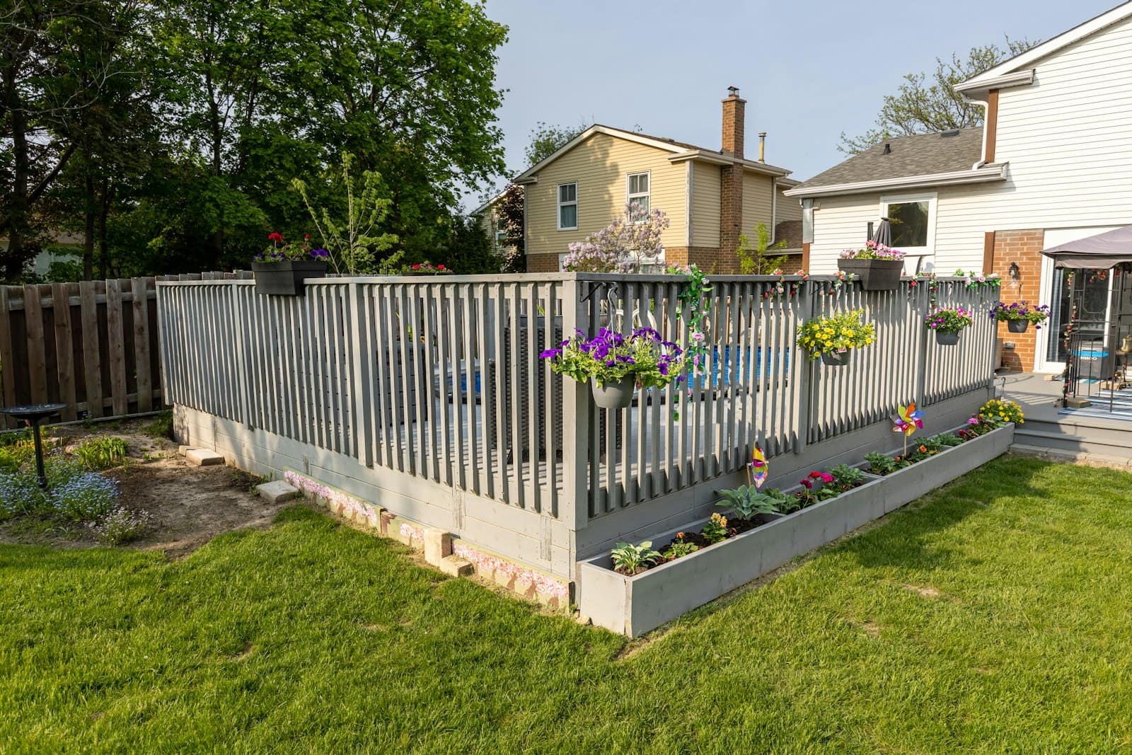 A mown backyard lawn beside a raised deck and fence, with two-storey neighbouring houses showing above the fence line.