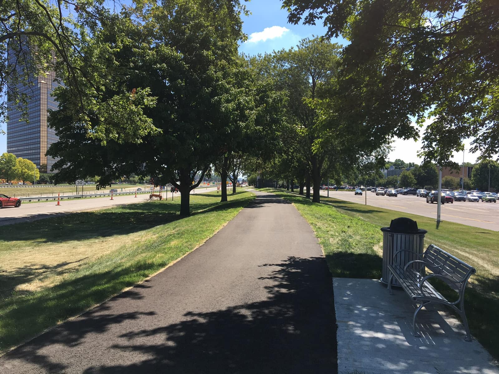 A paved shared-use walking path lined with mature shade trees and a bench in the Southfield City Centre, Southfield, Michigan.